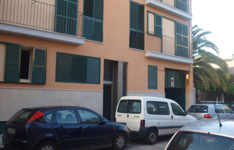 Fachada de un edificio de viviendas, se ven varios coches aparcados