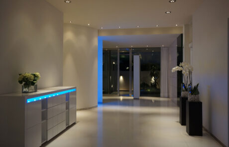 Interior de la segunda planta una vivienda, se ven dos orquídeas y una mueble en blanco con iluminación en azul