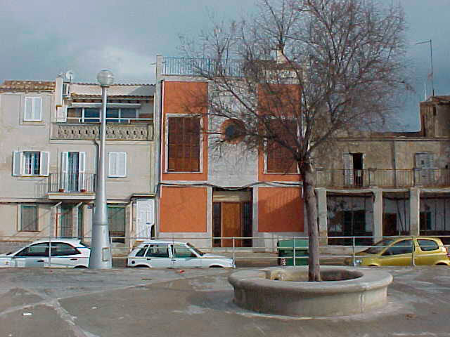 fachada de una iglesia convertida en vivienda, se ve también la plaza con un árbol