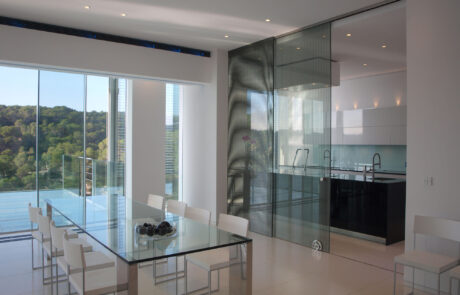 Comedor / cocina de una vivienda, al fondo cocina totalmente equipada separada del comedor por puertas correderas de cristal. En el comedor se puede ver una mesa de cristal con sillas.